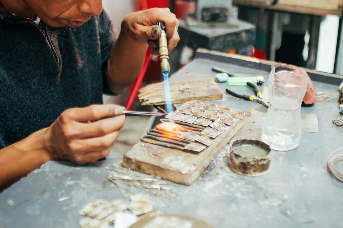 Banco de taller con soplete, pinzas y pequeñas piezas de metal preparadas para esmaltar